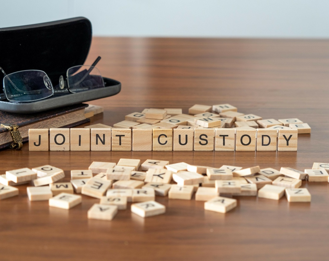 joint custody word or concept represented by wooden letter tiles on a wooden table with glasses and a book